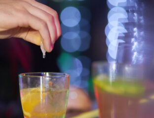 Shown is a person's hand dropping an unknown substance into someone's drink.