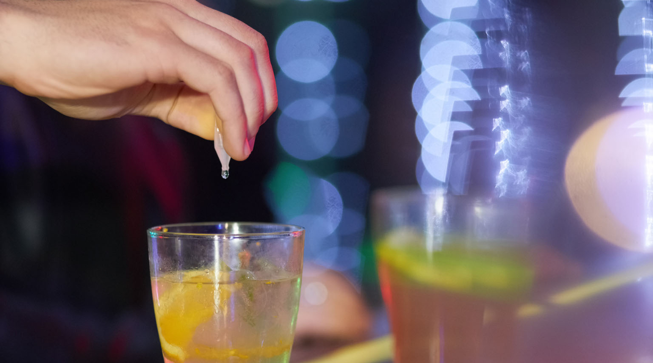 Shown is a person's hand dropping an unknown substance into someone's drink.